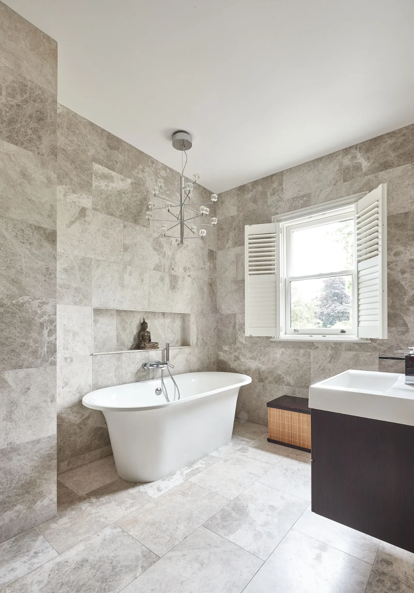 Silver marble tiled bathroom with freestanding bath and stone niche