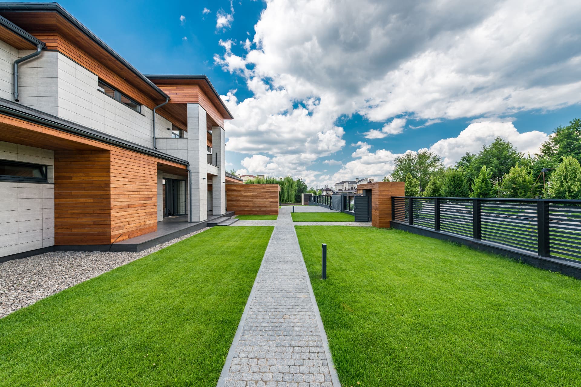 Manicured lawn with granite sett pathway alongside a contemporary timber and stone house