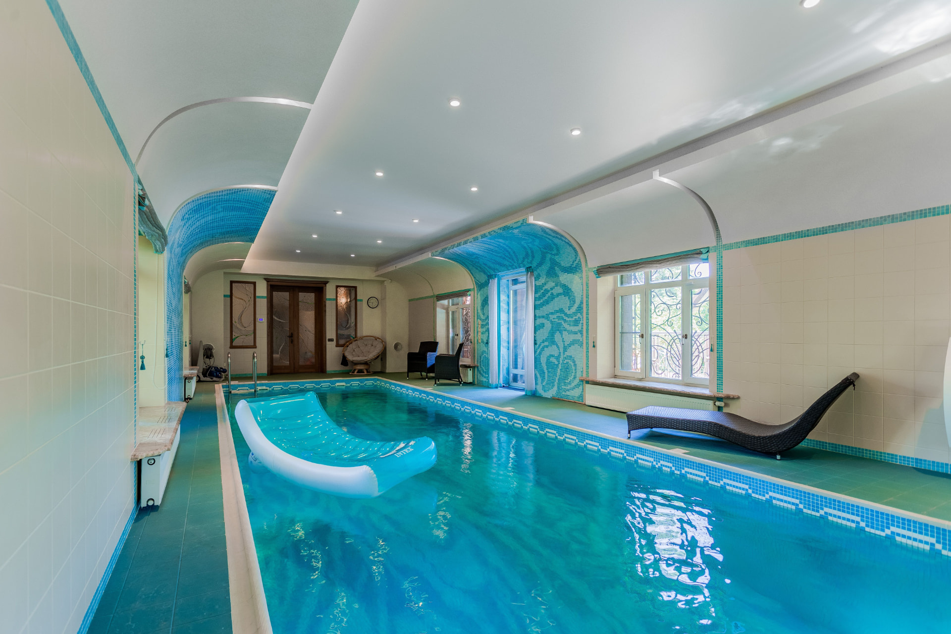 Vaulted indoor villa pool hall with mosaic-lined arches and turquoise water