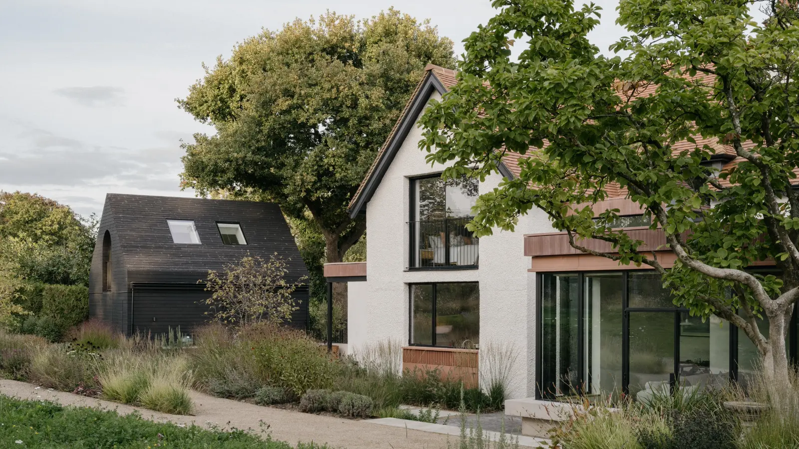 Landscaped meadow garden to a rendered house and black timber studio