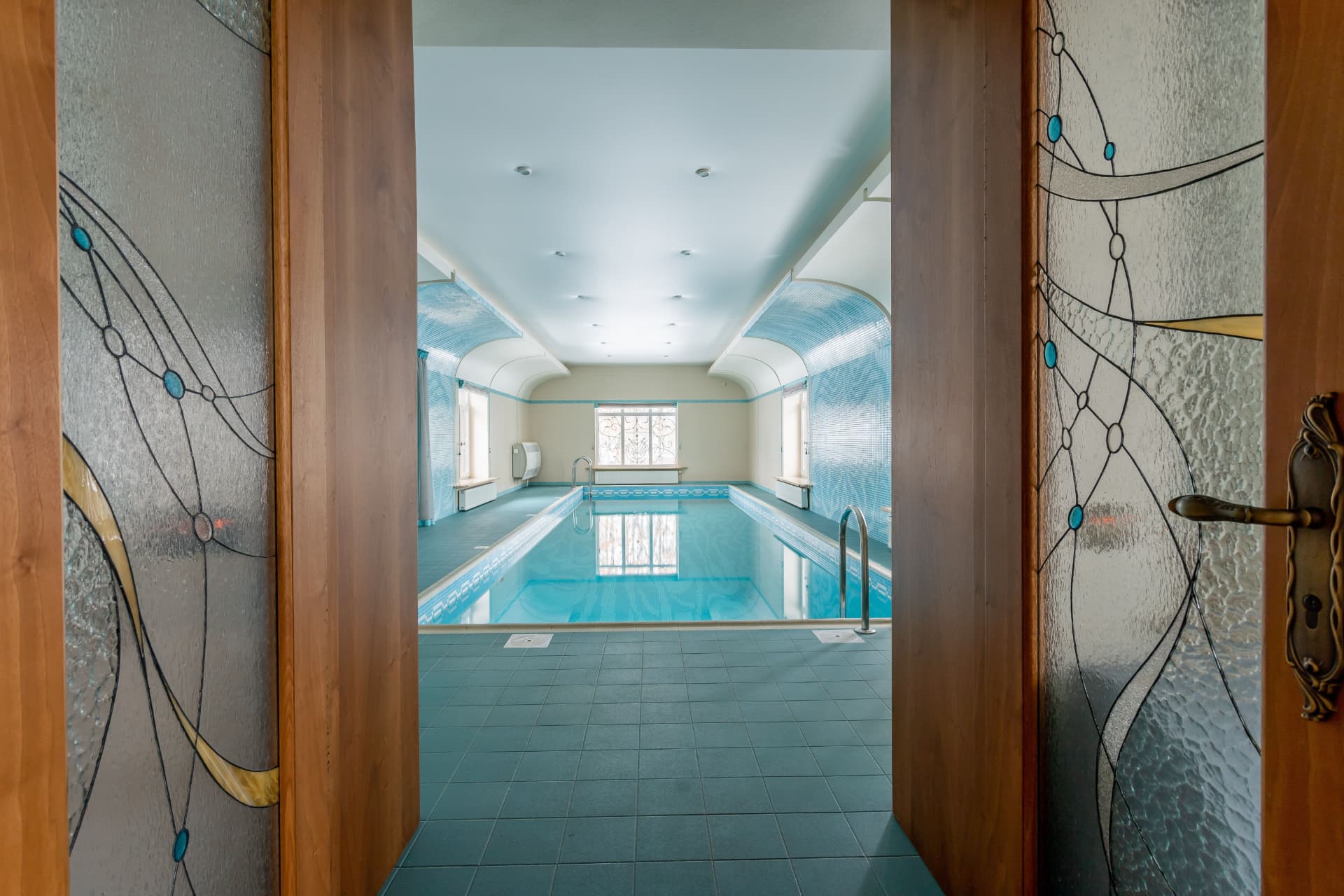 View through stained-glass timber doors into the finished indoor pool hall