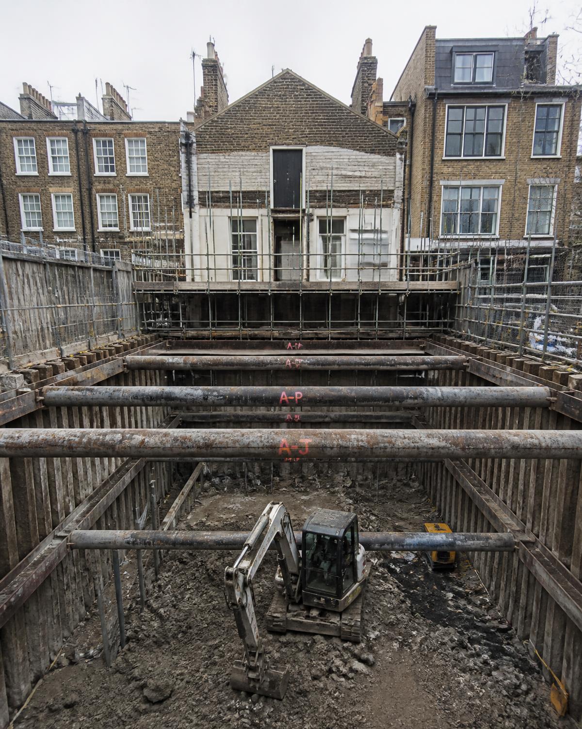 Propped basement dig with excavator loading spoil at Battersea