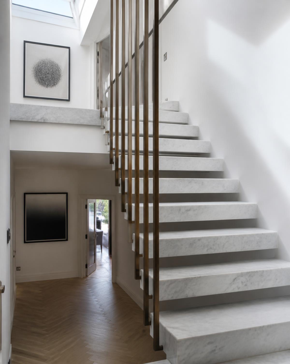 Floating marble treads with slim bronze balustrade under a rooflight